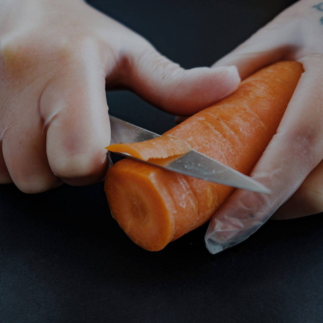 Person peeling a carrot with a knife on a dark surface