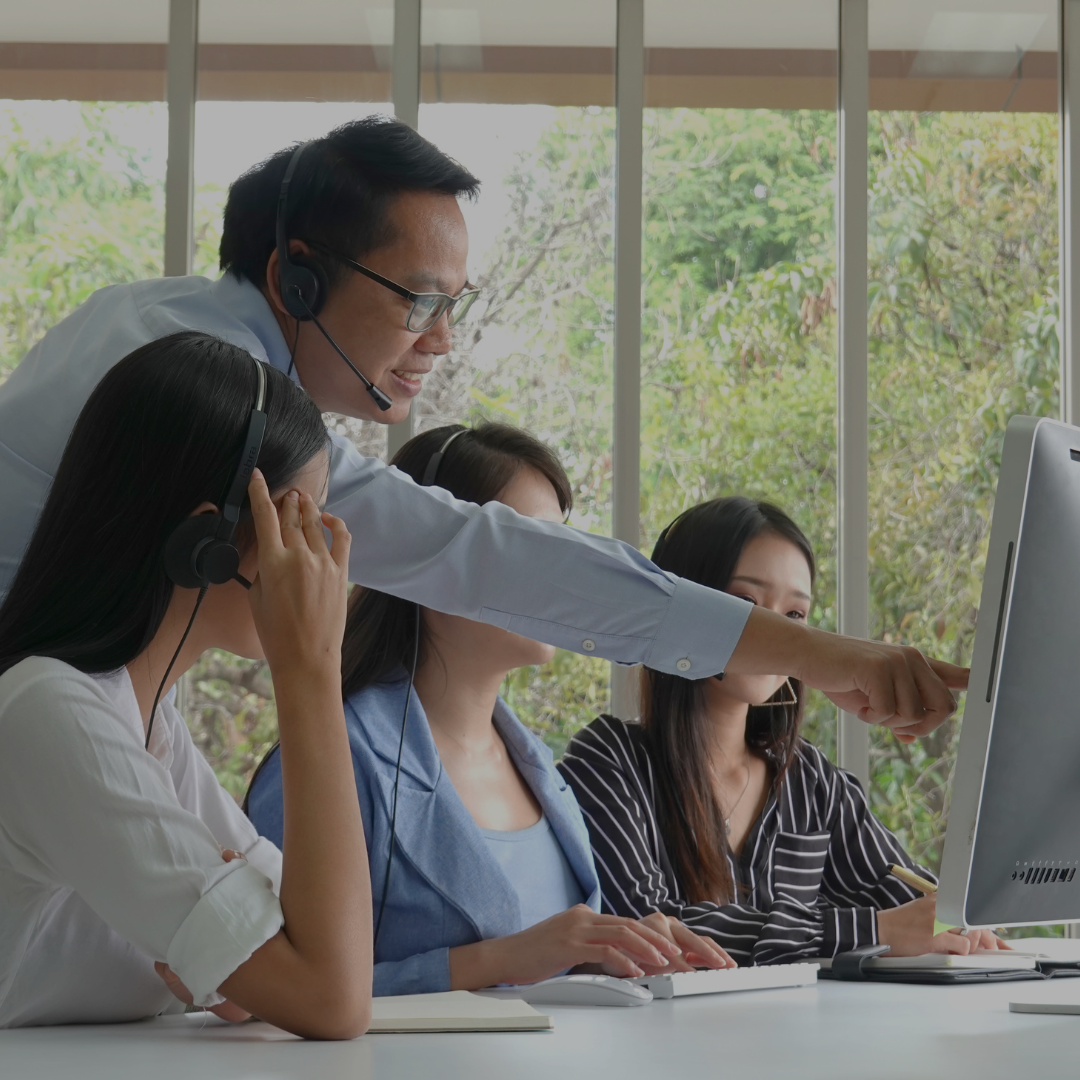 Manger pointing at a computer screen to help staff with headsets on
