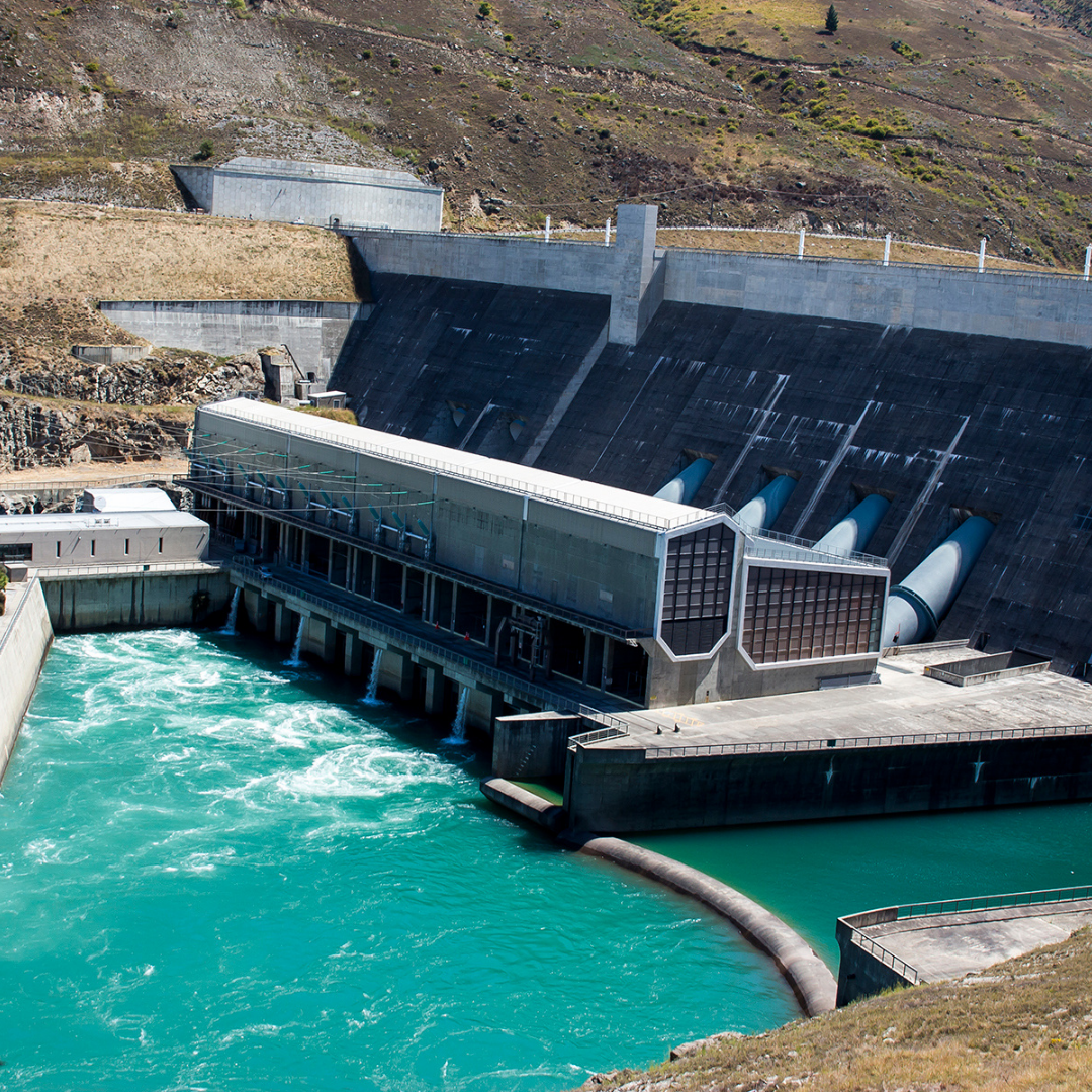 Large dam with water flowing through it, surrounded by a mountainous landscape.