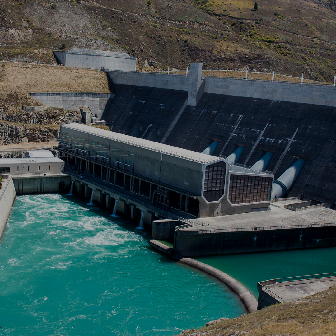 Large concrete dam with water flowing over it, surrounded by a natural landscape.