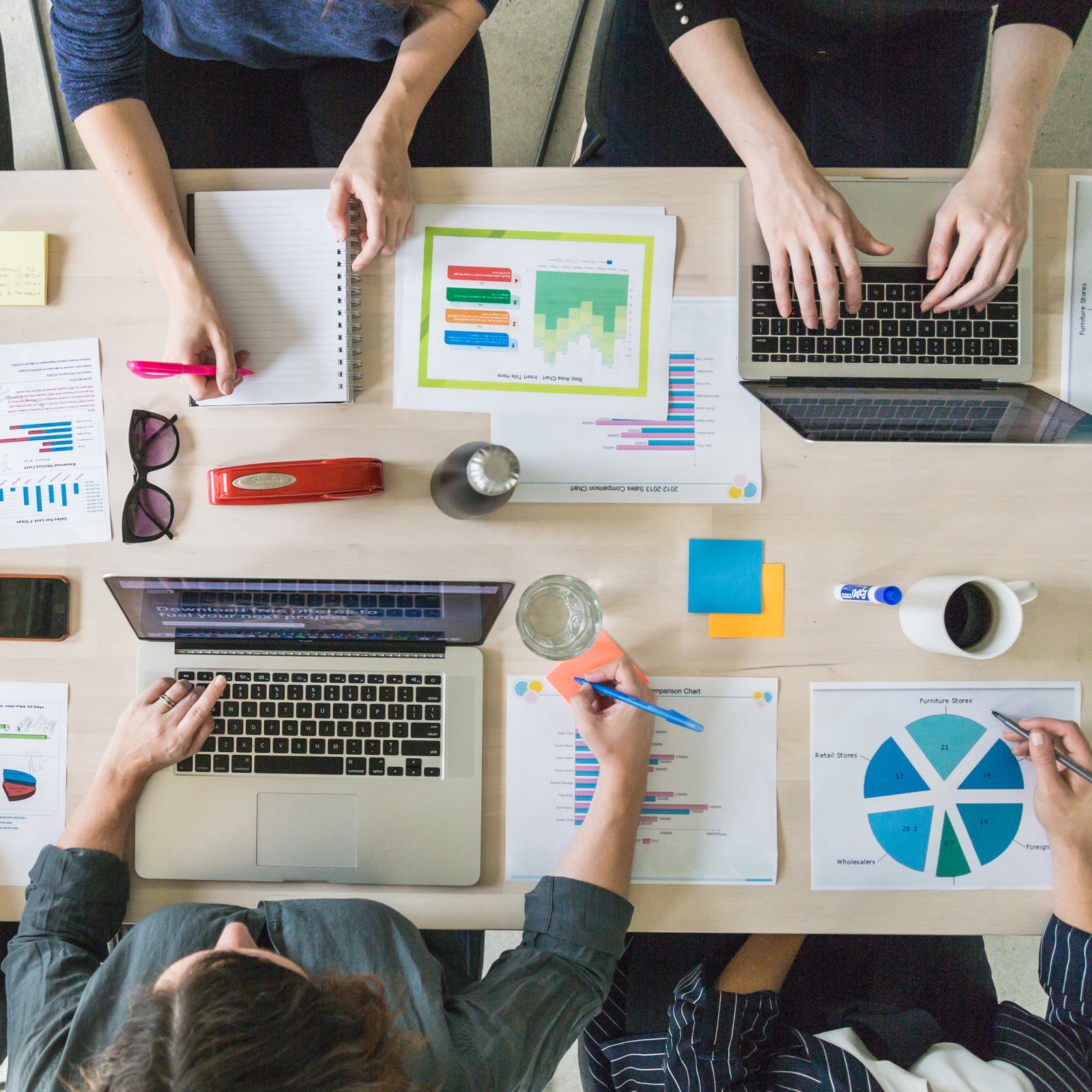 Top down shop of four office workers collaborating on paper and computers